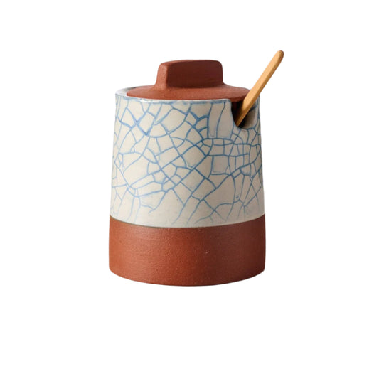 Ceramic container with textured lid and wooden spoon on a light background